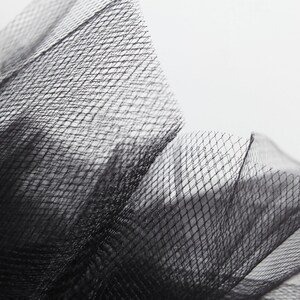 Peut inclure: Gros plan sur un tissu de tulle noir avec un motif en maille fine. Le tissu est doux et d&eacute;licat, avec une surface l&eacute;g&egrave;rement textur&eacute;e.
