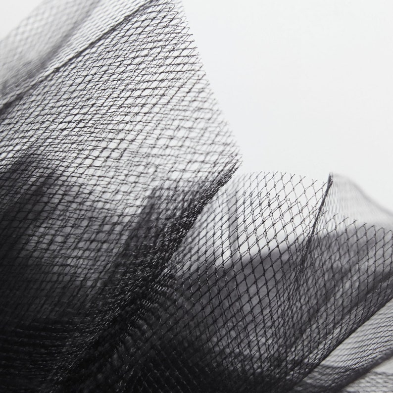 Peut inclure: Gros plan sur un tissu de tulle noir avec un motif en maille fine. Le tissu est doux et d&eacute;licat, avec une surface l&eacute;g&egrave;rement textur&eacute;e.