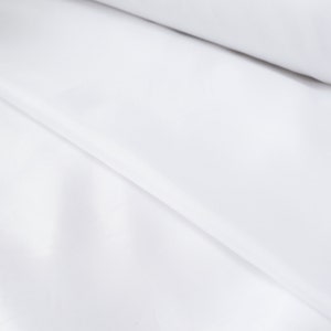 May include: White fabric with a smooth texture and a subtle sheen. The fabric is folded in a diagonal pattern, creating a soft, flowing look.