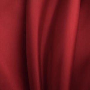 Könnte beinhalten: Nahaufnahme eines tiefroten Stoffes mit weichen Falten und subtilen Lichtreflexen. Das Material wirkt glatt und drapiert sich anmutig, wodurch ein Gefühl von Tiefe und Textur entsteht. Die satte Farbe deutet auf ein luxuriöses Textil hin.