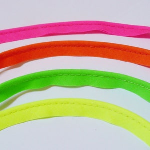 May include: Four different colours of bias tape, pink, orange, green, and yellow, are shown in a semi-circle shape. The tape is sewn with a straight stitch.