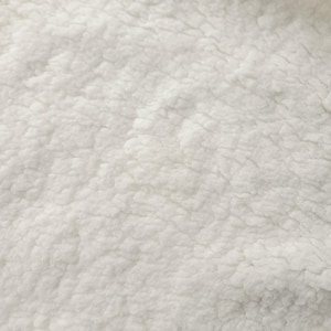 Puede incluir: Primer plano de una tela blanca texturizada con una apariencia suave y afelpada. La superficie está cubierta de pequeños bultos irregulares, creando un aspecto acogedor y atractivo. El material parece ser un tipo de forro polar o sherpa.