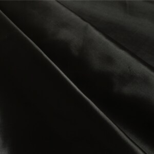 May include: Black satin fabric with a smooth, silky texture. The fabric is folded in half, creating a diagonal crease.