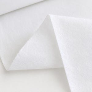 Könnte beinhalten: Ein Stück einfarbiger, weißer Stoff mit einer weichen, leicht flauschigen Textur. Das Material ist so gefaltet, dass eine scharfe, dreieckige Spitze entsteht, die die gleichmäßige, opake weiße Farbe und die feine, faserige Oberfläche zeigt.