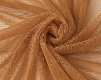 May include: A sheer, light brown fabric with a fine, open-weave mesh texture. The material is gathered in a central spiral, creating soft, radiating folds and drapes that highlight the translucent quality and the consistent tan colour of the textile.
