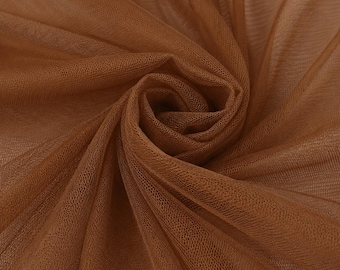 May include: A sheer, lightweight fabric in a warm, medium-brown tone. The material features a fine, grid-like mesh texture and is gathered into a central swirl, creating soft, flowing folds and shadows that highlight the translucent quality.