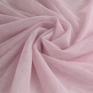 May include: Close-up of a soft, light pink tulle fabric. The fabric is gathered and draped, creating folds and shadows. The delicate material has a sheer, airy appearance, ideal for crafting or decorative purposes.
