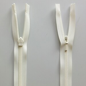May include: Two white zipper pulls with a silver slider. The zippers are open and the slider is in the middle of the zipper.