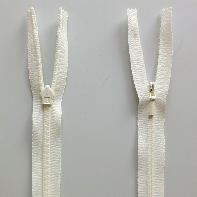 May include: Two white zipper pulls with a silver slider. The zippers are open and the slider is in the middle of the zipper.