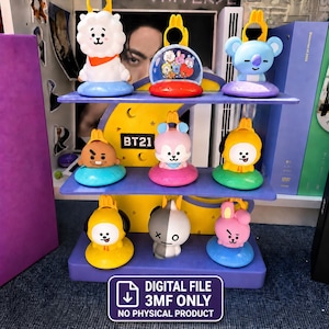 May include: A three-tiered purple display stand featuring a yellow crescent moon cutout with the text BT21. Eight colorful character figurines are arranged on the shelves, each with a yellow loop on top. A sign reads DIGITAL FILE 3MF ONLY NO PHYSICAL PRODUCT.