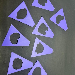 Pode incluir: Uma cole&ccedil;&atilde;o de oito est&ecirc;nceis de pl&aacute;stico roxo, cada um em forma de tri&acirc;ngulo com um design recortado exclusivo no centro. Os recortes apresentam v&aacute;rias formas, incluindo contornos arredondados, formas de nuvens e silhuetas org&acirc;nicas irregulares.