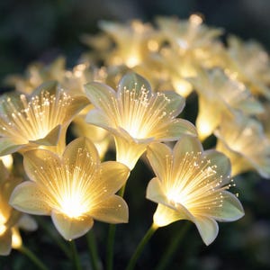 May include: A cluster of artificial lily-shaped flowers featuring pale yellow petals and illuminated fiber optic stamens that emit a warm white glow. Each flower is attached to a thin green stem, creating a bright, glowing floral arrangement.
