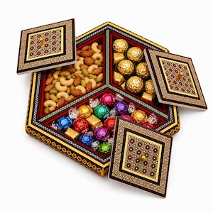 May include: A hexagonal wooden serving tray with three internal compartments, each covered by a removable square lid featuring intricate geometric patterns in red, gold, and black. The tray holds assorted nuts and colorful foil-wrapped chocolates.
