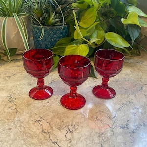 May include: Three matching ruby red glass goblets with a faceted, geometric bowl design and a sturdy, multi-sided stem. Each glass features a wide, circular base and a deep, vibrant red color throughout the translucent glass material.