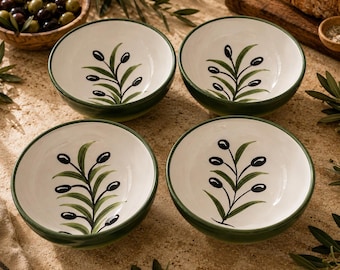 May include: A set of four round ceramic bowls with a cream-colored interior and a dark green rim. Each bowl features a hand-painted design of a green olive branch with black olives centered on the bottom. The bowls have a smooth, glossy finish.