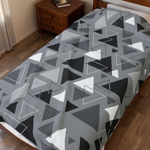 May include: A bedspread featuring a repeating geometric pattern of triangles in shades of black, white, and various tones of gray. Some triangles are solid, while others are outlined or filled with fine parallel line textures across the fabric.