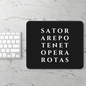 Puede incluir: Una alfombrilla de ratón rectangular negra con el texto blanco del cuadrado Sator en una fuente con serifa. El texto está dispuesto en cinco filas: SATOR, AREPO, TENET, OPERA y ROTAS. La alfombrilla tiene un borde cosido y está junto a un teclado blanco.