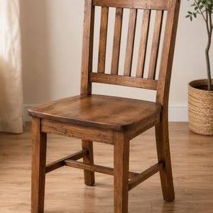 May include: A wooden chair with a medium brown finish, featuring a slatted backrest with five vertical slats, a flat square seat, and four straight legs connected by horizontal support stretchers on the sides and front for added stability.