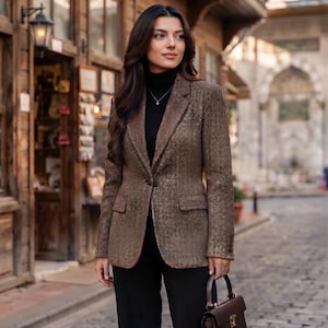 May include: A brown textured blazer with a notched lapel and two front flap pockets, worn over a black turtleneck jumper and black trousers, accompanied by a structured dark brown leather handbag with a top handle and a gold-toned metal clasp.