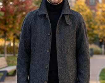 May include: A charcoal gray herringbone patterned overcoat featuring a structured collar, long sleeves, and a front button closure. The coat is worn over a solid black turtleneck sweater, creating a layered look with a classic, straight-cut silhouette.