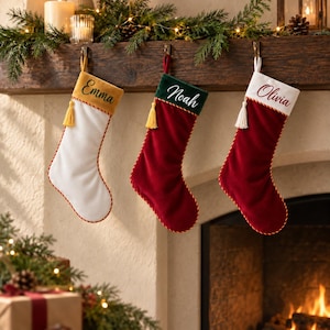 Könnte beinhalten: Drei personalisierte Weihnachtsstrümpfe hängen in einer Reihe. Der erste ist weiß mit goldenem Umschlag und gelber Quaste, beschriftet mit Emma. Der zweite ist rot mit grünem Umschlag und gelber Quaste, beschriftet mit Noah. Der dritte ist rot mit weißem Umschlag und weißer Quaste, beschriftet mit Olivia.