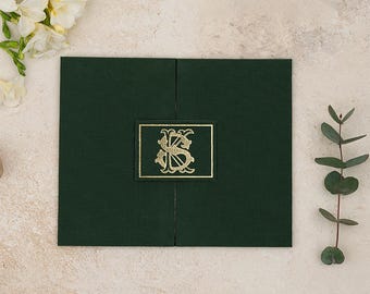 May include: A dark green rectangular gatefold invitation folder featuring a central rectangular plaque with a gold foil embossed monogram of the letters KS. The folder has a textured fabric-like finish and is closed in the center.
