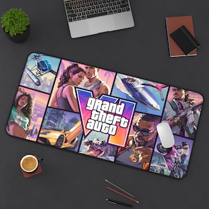 May include: A rectangular desk mat featuring a collage of Grand Theft Auto game art. The design includes characters, a yellow sports car, a speedboat, a helicopter, and an alligator, centered around the Grand Theft Auto logo in purple and orange.