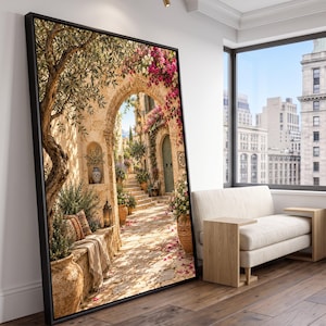 May include: A large framed wall art print depicting a sunlit Mediterranean stone courtyard with an arched entryway, a gnarled olive tree, vibrant pink bougainvillea flowers, terracotta pots, a stone bench with a patterned cushion, and a lantern.