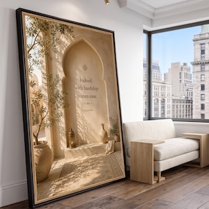 May include: A large framed wall art piece featuring a beige architectural archway with a potted olive tree, a lantern, and a vase. The text reads: Indeed, with hardship comes ease. Quran 94:6. The artwork is displayed in a black frame with a light wood trim.