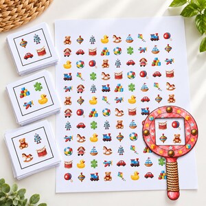 May include: A set of three stacks of square cards and a large rectangular sheet, all featuring colourful illustrations of toys like teddy bears, robots, rubber ducks, trains, and cars. A round magnifying glass tool with a red star pattern is included.
