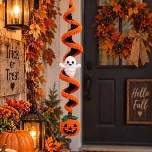 May include: A hanging crochet decoration featuring a spiral of orange and black yarn. A small white ghost with black eyes and a smile is attached to the centre of the spiral, and a round orange pumpkin with a green stem hangs at the bottom.