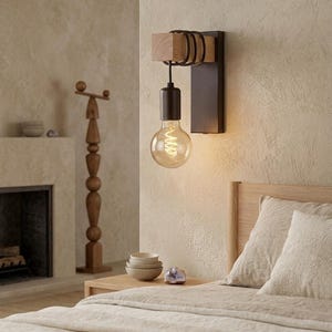 Peut inclure: Une applique murale composée d'une plaque arrière en métal sombre, d'un bloc de bois clair et d'un cordon noir enroulé autour du bois. Une douille noire supporte une grande ampoule ronde en verre transparent avec un filament lumineux visible.