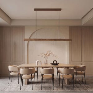 Puede incluir: Una lámpara colgante lineal de madera suspendida por cables finos sobre una mesa de comedor rectangular. La mesa está rodeada por seis sillas tapizadas en color beige con patas finas de metal negro. Un jarrón de cristal con ramas secas.