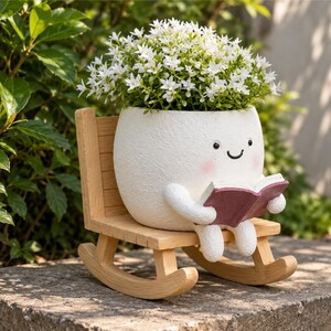 May include: A white, textured, round planter shaped like a character with a smiling face and pink cheeks, sitting on a light-colored wooden rocking chair. The planter holds a cluster of small white flowers and holds an open maroon book.