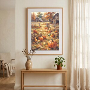 Könnte beinhalten: Ein gerahmter Kunstdruck, der eine herbstliche ländliche Landschaft zeigt, mit orangefarbenen Kürbissen auf einem Feld aus trockenem Gras und Heuballen, sowie verwitterten Holzscheunen, einem rustikalen Zaun und Bäumen mit goldenem Laub.