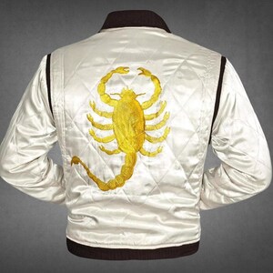 May include: A white quilted satin bomber jacket featuring a large, detailed gold embroidered scorpion on the back. The jacket has a dark brown ribbed collar, cuffs, and hem, with a diamond-stitched pattern across the white fabric panels.