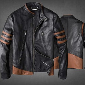 Könnte beinhalten: Eine schwarze Jacke mit braunen Akzenten, ausgestattet mit einem Stehkragen, einem Frontreißverschluss und drei horizontalen braunen Streifen an jedem Ärmel. Die Jacke verfügt über zwei vertikale Reißverschlusstaschen vorne und ein braunes Paneel am Saum.