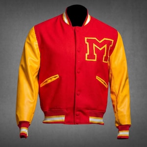 Könnte beinhalten: Eine rote Collegejacke mit gelben Ärmeln und einem großen gelben Buchstaben M auf der linken Brust. Die Jacke verfügt über eine Druckknopfleiste, zwei gelb eingefasste Seitentaschen sowie einen gerippten Kragen und Bündchen mit weiß-gelben Streifen.