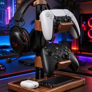 May include: A wooden and black metal gaming organizer stand featuring a top hook for black over-ear headphones, two tiered cradles holding a white and a black game controller, and a rectangular base tray containing a white earbud case and a smartphone.
