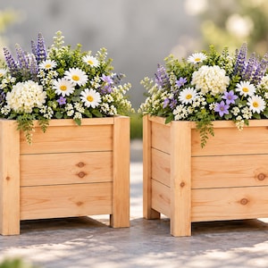 Op de afbeelding: Twee vierkante houten plantenbakken gemaakt van lichtgekleurde horizontale planken met stevige hoekpalen. Elke plantenbak is gevuld met een levendig arrangement van witte madeliefjes, paarse lavendelachtige aren, witte hortensia's en groen blad.