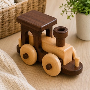 May include: A wooden toy train engine featuring a dark brown walnut wood cabin and base, contrasted with a light-colored natural wood boiler and four round wheels. The locomotive includes a cylindrical smokestack and small wooden pegs.