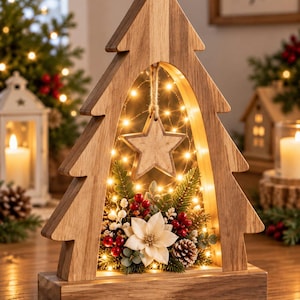 May include: A wooden Christmas tree-shaped decoration with a hollow center containing a hanging wooden star, warm fairy lights, a white poinsettia, red berries, green pine needles, and a small pinecone, all mounted on a rectangular wooden base.