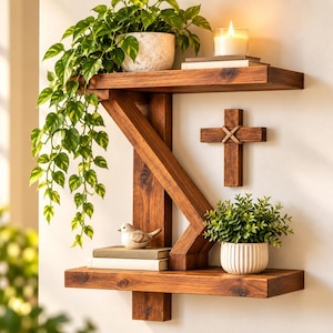 May include: A two-tier wall-mounted wooden shelf with a dark brown finish. The top shelf holds a trailing green plant in a textured pot and a lit candle on a book. The bottom shelf features a small bird figurine, books, and a green plant in a ribbed pot.
