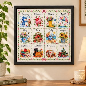 May include: A framed wall art piece featuring a twelve-month calendar grid. Each month displays a seasonal illustration: a snowman, hearts, flowers in a boot, an umbrella, a watering can, a berry basket, a beach chair, sunflowers, books, a cat with a pumpkin, a mug, and a Christmas tree.