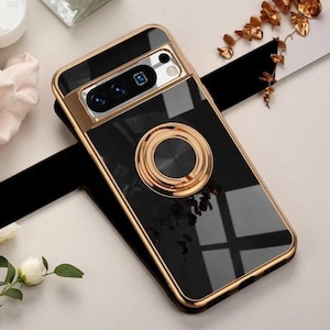 May include: A glossy black smartphone case featuring a metallic gold frame and a matching gold circular ring stand centered on the back. The camera module area is also outlined in gold, highlighting the lens cutouts on this protective cover.