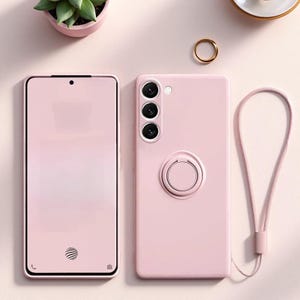 May include: A light pink smartphone case with a matching circular ring holder on the back and a thin wrist strap attached to the side. The case features three camera lens cutouts and a small flash opening, providing a sleek, solid-colored cover.