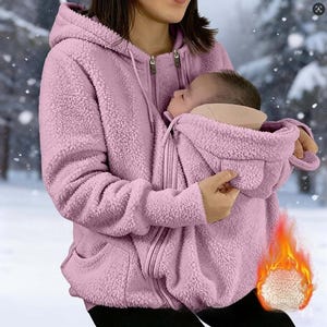 May include: A light purple, long-sleeved, zip-up hoodie made of textured fleece material. The garment features a hood with drawstrings and a specialised front pouch section designed to accommodate a baby, complete with its own small hood.