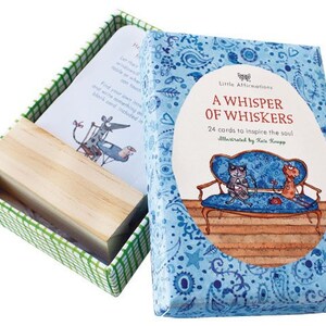 May include: A blue box with a paisley pattern and the text "Little Affirmations A Whisper of Whiskers 24 cards to inspire the soul Illustrated by Kate Knapp" on the front. The box contains a set of affirmation cards with illustrations of cats.