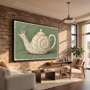 May include: A framed wall art print featuring a cream-coloured teapot shaped like a snail with a spiral shell body, a curved handle, and a spout with two eye-like protrusions. The teapot is decorated with small blue polka dots on a sage green background.