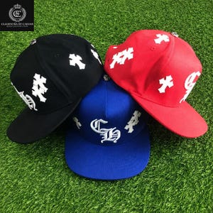 May include: Three baseball caps in black, blue, and red, each featuring white embroidered cross patches and white lettering. The black cap has a cross pattern, the blue cap displays the letters CH, and the red cap features crosses and white text.